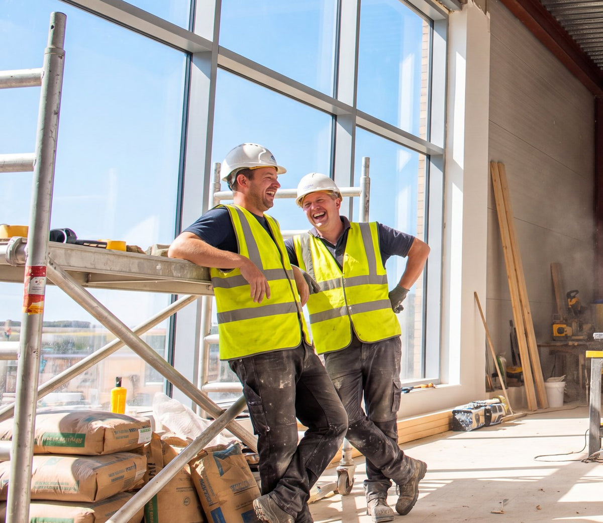 Two tradesmen in hi-vis laughing on a bright interior building site